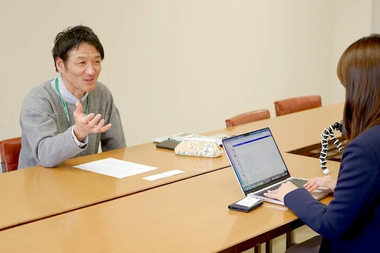 会議室でインタビューを受ける岡崎氏と、ノートPCで記録する尾勢